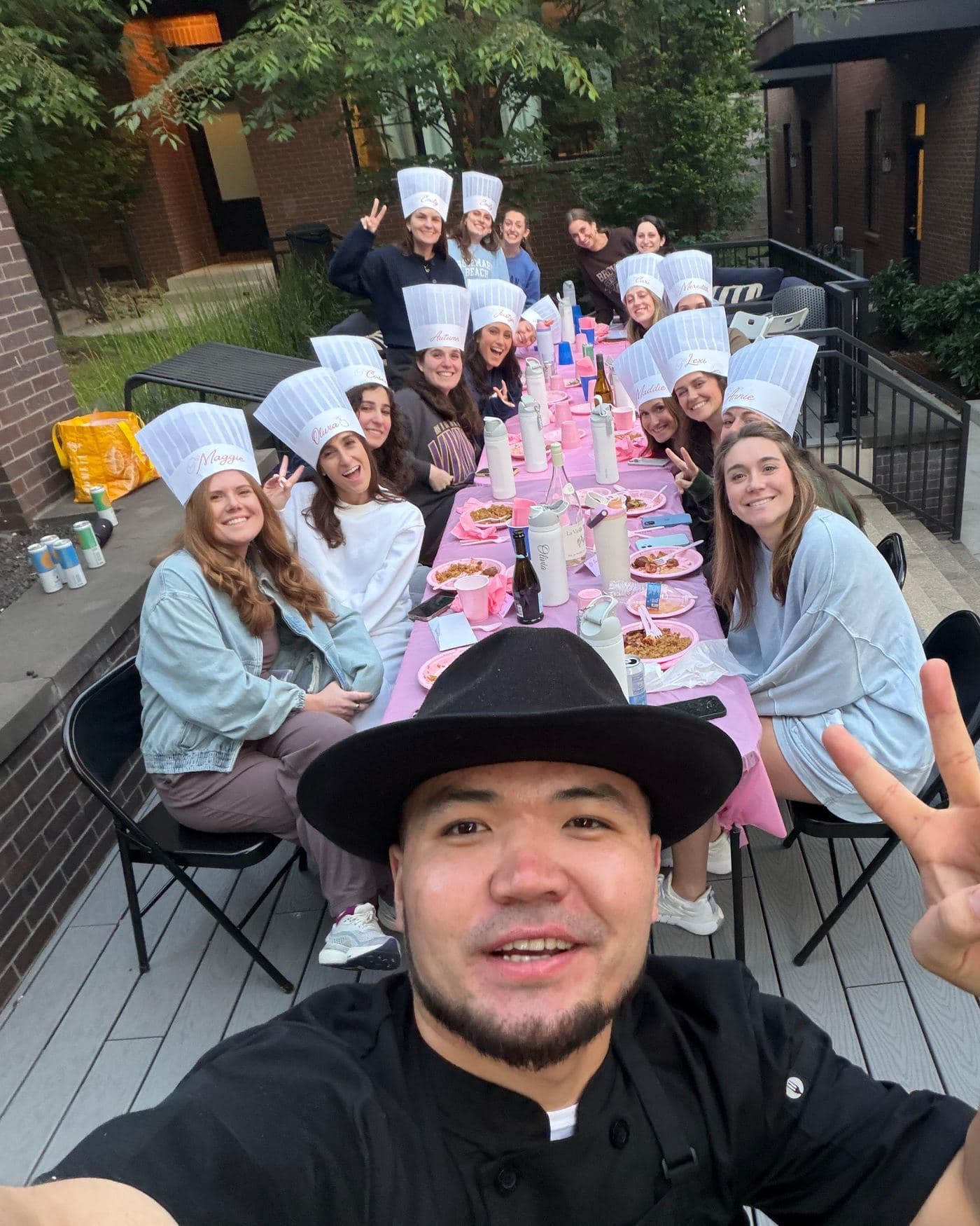Our chef in his black coat and hat taking a selfie with a full table of guests wearing paper chef hats