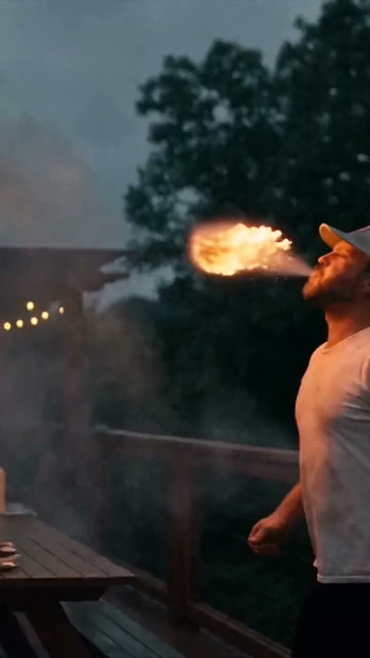 Our chef breathing a fireball over a backyard deck at dusk, mountains behind